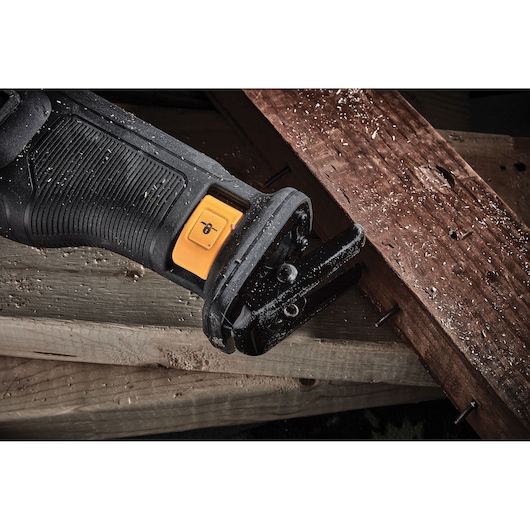 Close-up of a DEWALT reciprocating saw cutting through wood with embedded nails.