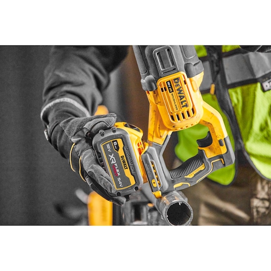 Worker uses a yellow DEWALT cordless reciprocating saw on a metal pipe.