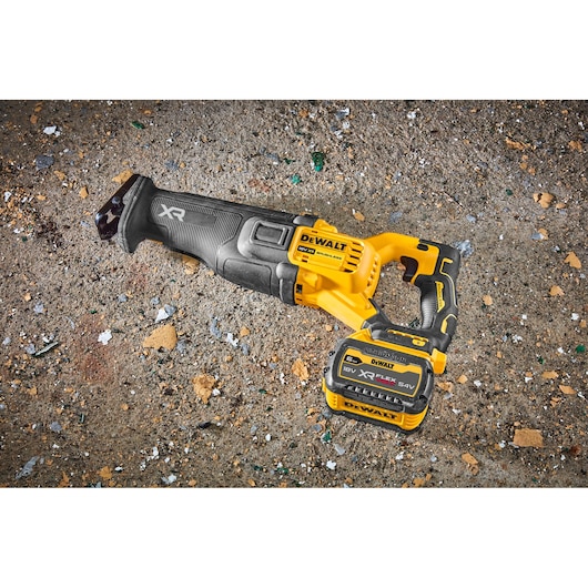 DEWALT cordless reciprocating saw with battery, placed on a rough concrete surface with debris.