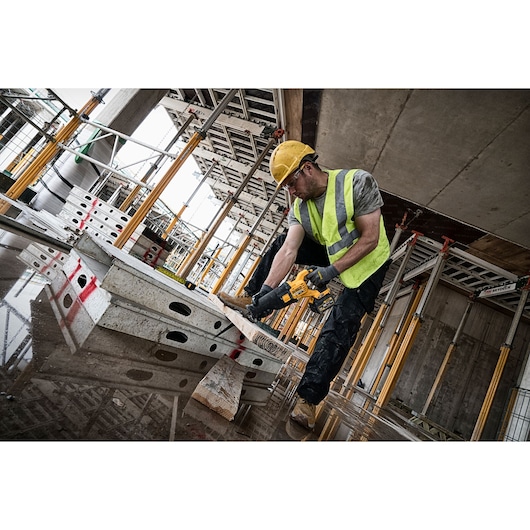Worker using DEWALT DCS388N saw to cut wood at a construction site with safety gear and high-vis vest.
