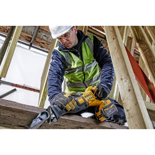 Worker using a DEWALT DCS389NT reciprocating saw on wood at a construction site.