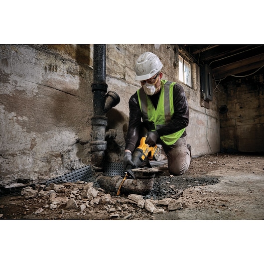Worker in safety gear uses DEWALT tool to cut a pipe in a rough, indoor construction site.