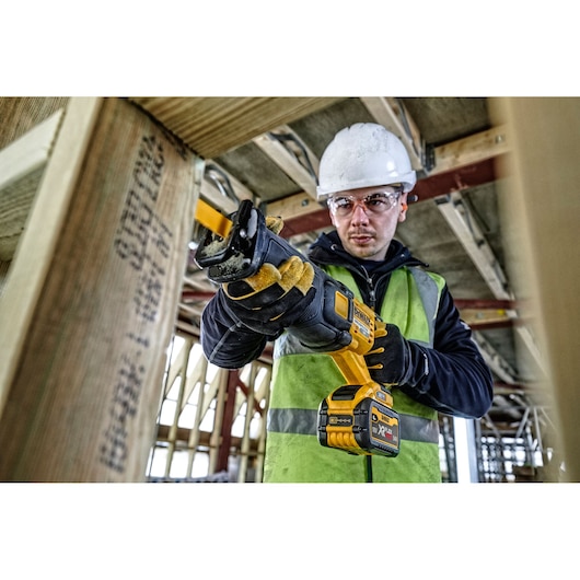 Worker using a DEWALT cordless reciprocating saw to cut wood at a construction site.