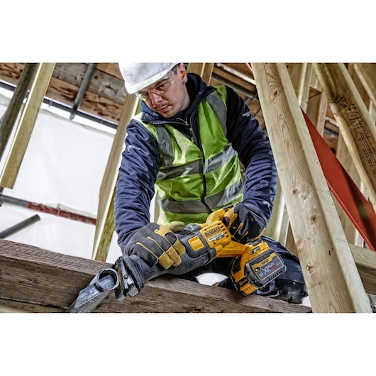 Worker uses DEWALT DCS389T2 cordless saw to cut wood on a construction site. Face is blurred for privacy.