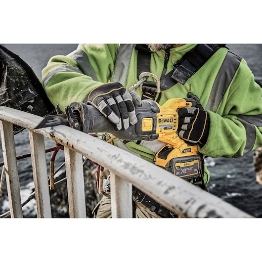 Worker uses a DEWALT cordless reciprocating saw to cut a metal railing outdoors.