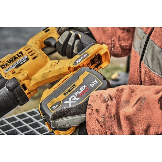 DEWALT XR FlexVolt 54V power tool battery held by gloved hands during outdoor work.
