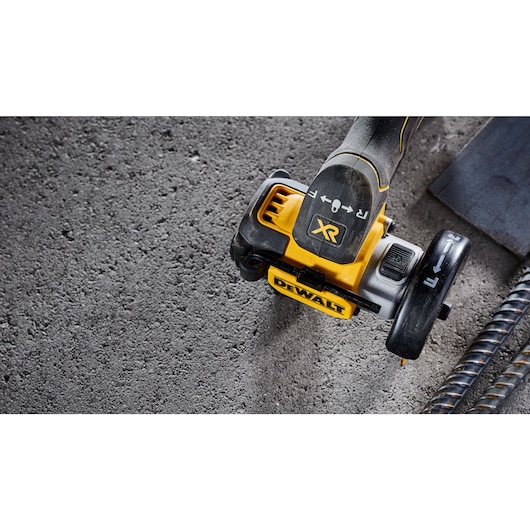 Close-up of a DEWALT DCS438N power tool with XR branding, shown on a rough concrete surface alongside metal rods.