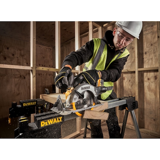Worker uses DEWALT DCS565P2 circular saw to cut wood on a stand in a construction site.