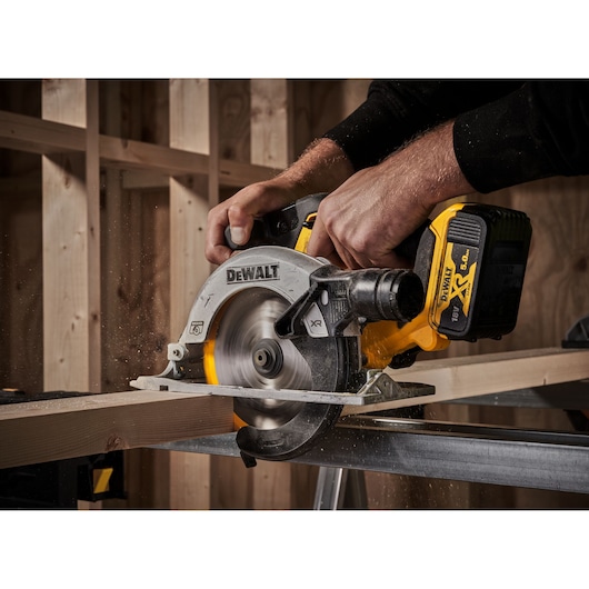 DEWALT cordless circular saw cutting wood plank in a workshop with hands operating the tool.