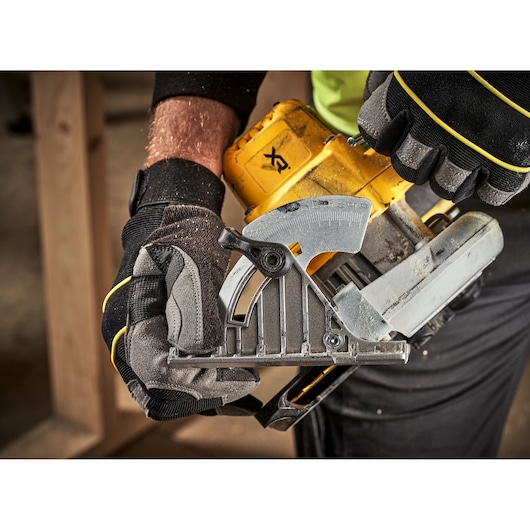 Gloved hands adjust a yellow DEWALT circular saw, focusing on the angle gauge and saw mechanism.