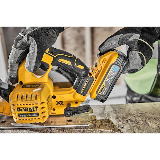Gloved hands attach a DEWALT 18V battery to a yellow cordless saw on a workbench.