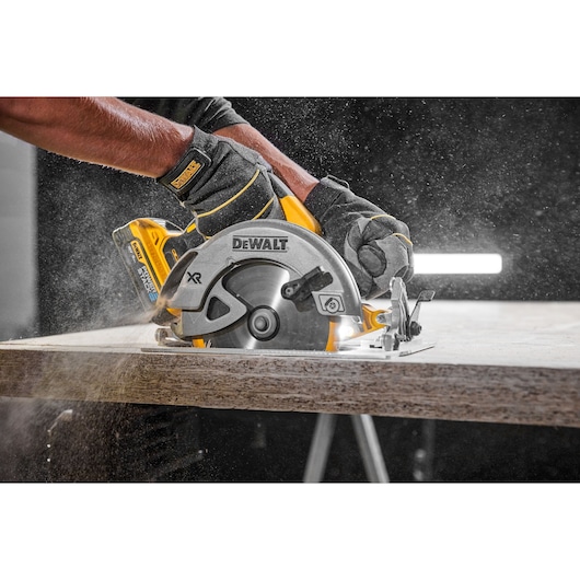 Person using a DEWALT cordless circular saw to cut wood. Sawdust is visible as the tool operates.