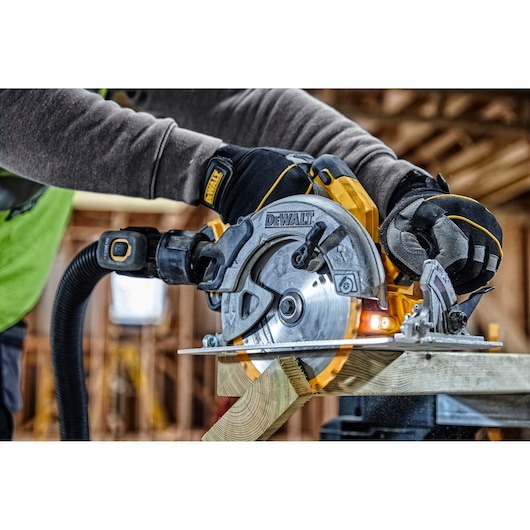 A DEWALT circular saw cutting wood, held by a gloved worker on a construction site.