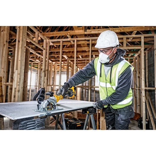 DEWALT DCS571NT-XJ, DCS571NT saw used by worker in construction setting. Safety gear worn. Photography category.