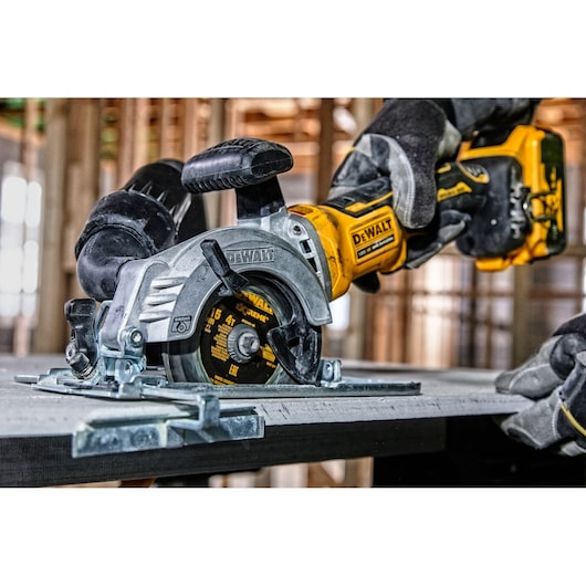DEWALT cordless circular saw cutting wood, operated by a gloved hand at a construction site.