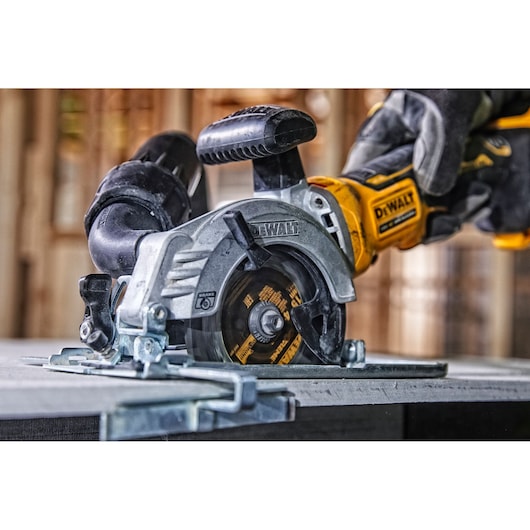 DEWALT cordless circular saw cutting wood, held by a gloved hand in a workshop.