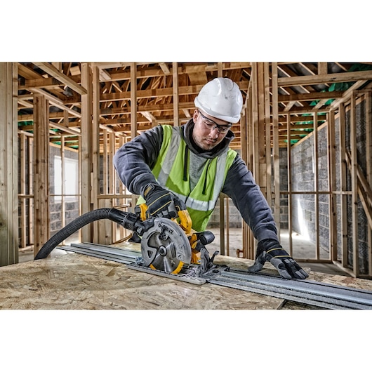 Worker uses a DEWALT circular saw with guide rail on wood inside a building under construction.