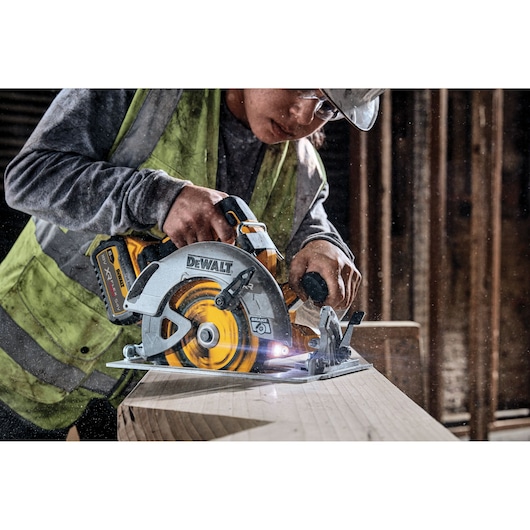 DEWALT cordless circular saw cutting wood, used by a worker wearing a vest in a construction setting.