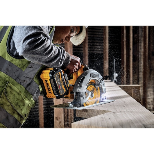 DEWALT cordless circular saw in use, cutting wood on a construction site. Sawdust visible around the blade.