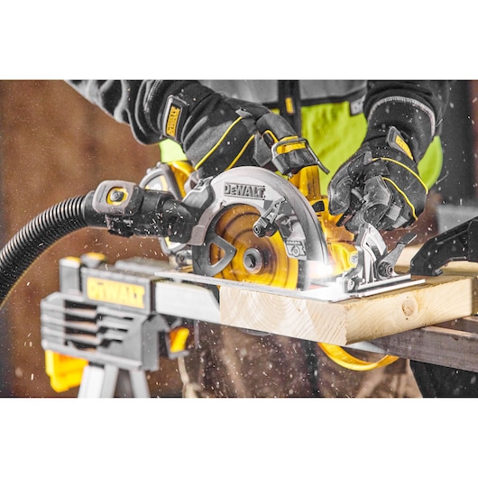 DEWALT circular saw in use cutting wood, worker wearing gloves and work gear, dust particles visible.