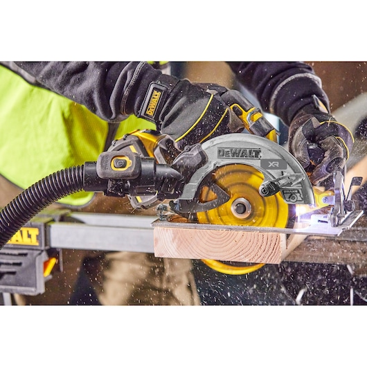 DEWALT circular saw in use, cutting wood while attached to a vacuum hose for dust extraction.