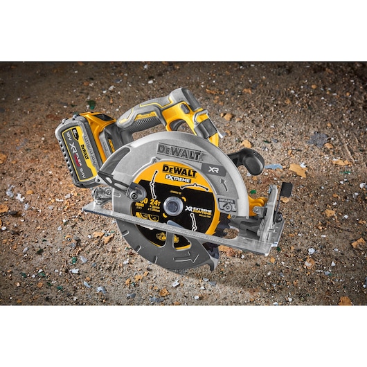 DEWALT cordless circular saw (model DCS573NT) with a visible battery pack and blade, placed on a rough construction site surface.