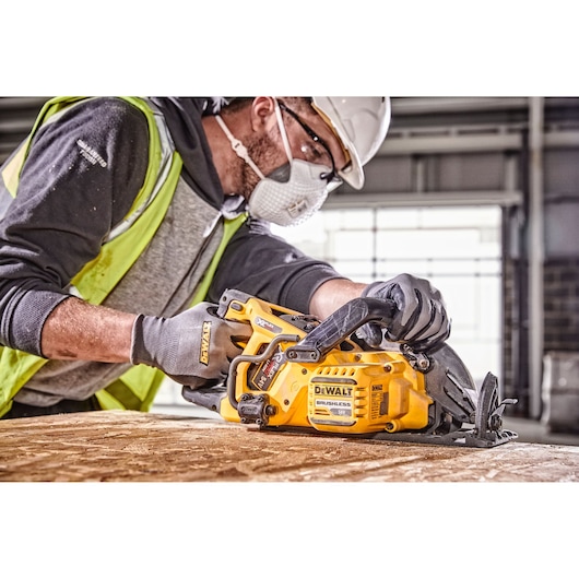 Person using a DEWALT DCS577N circular saw on wood in a workshop. Face is blurred for privacy.