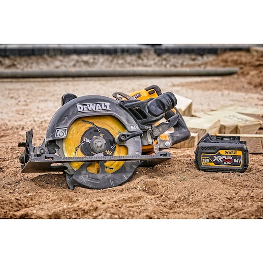 DEWALT cordless circular saw and battery on dirt, with wooden planks in background.
