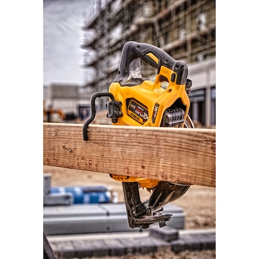 DEWALT DCS577N circular saw resting on wooden beam at a construction site, with scaffolding in the background.