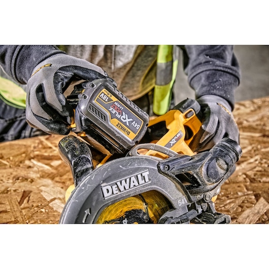 Person wearing gloves uses DEWALT cordless circular saw on a wooden surface.