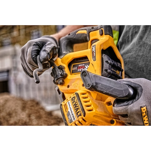 Close-up of gloved hands holding a yellow DEWALT cordless circular saw on a construction site.