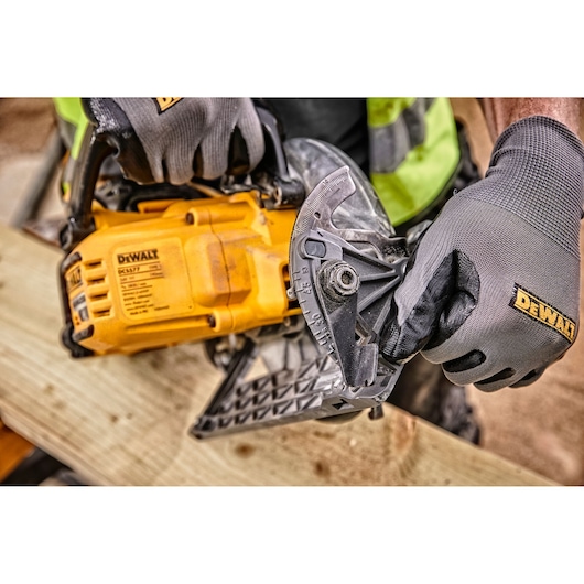 Person wearing gloves adjusts a DEWALT DCS577T2 circular saw on a wooden board at a construction site.