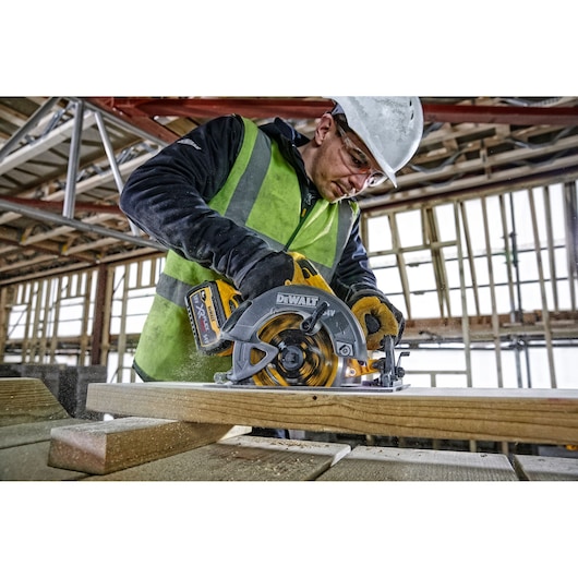 Worker using DEWALT DCS578NT circular saw to cut wood at a construction site.