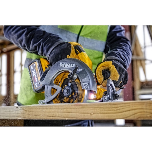 DEWALT cordless circular saw cutting wood, held by gloved hands in a construction setting.