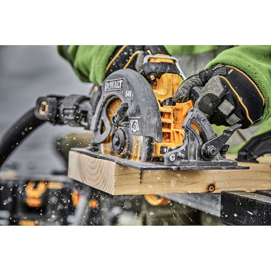DEWALT circular saw cutting wood, operated by gloved hands, sawdust flying in a workshop setting.