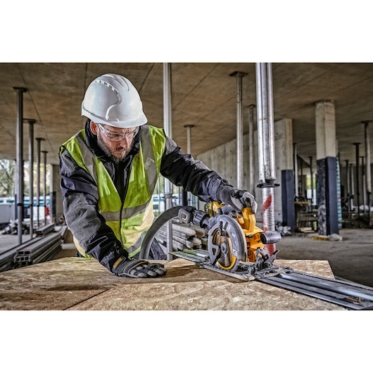 Worker uses a DEWALT circular saw to cut wood on a construction site, wearing safety gear and gloves.