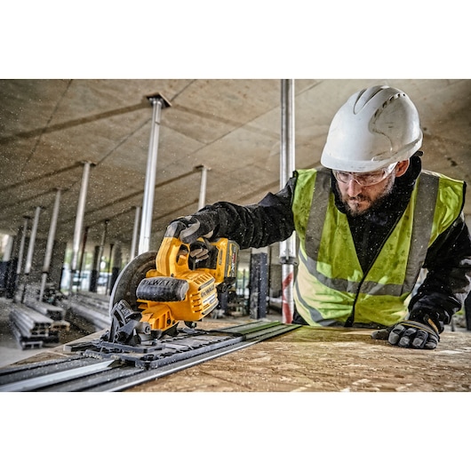 Worker uses DEWALT cordless circular saw, wearing safety gear, cutting wood at construction site indoors.