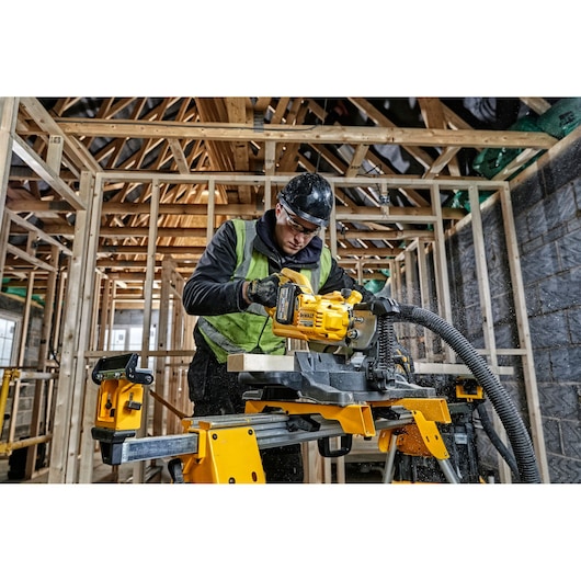 Person using a DEWALT cordless saw to cut wood inside a building under construction.