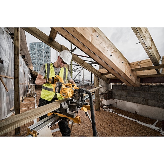 Worker uses DEWALT DCS777T2 saw to cut wood on construction site with safety gear and partially built roof.