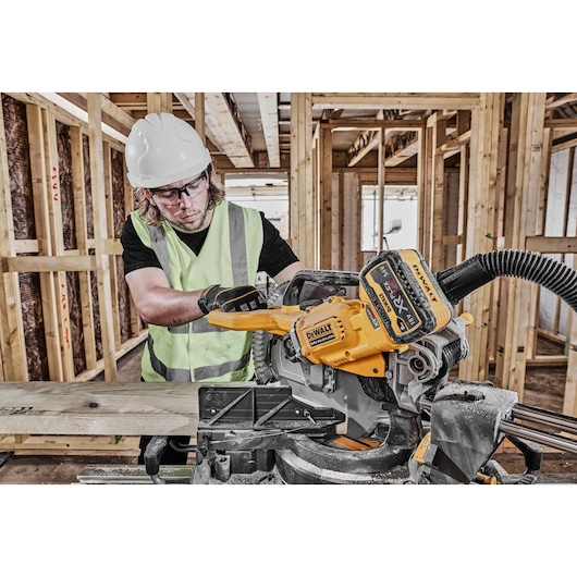 DEWALT DCS781N cordless saw used by worker in safety gear cutting wood at a construction site.