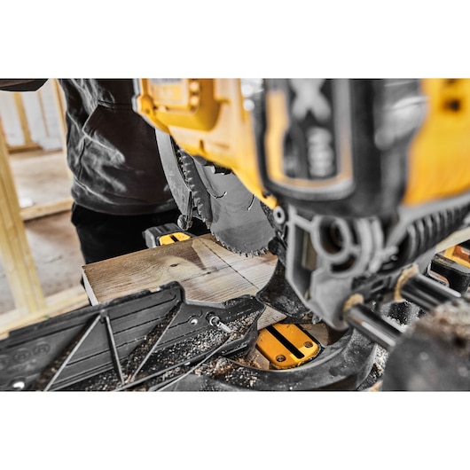 Close-up of a DEWALT miter saw cutting a wooden plank in a workshop.