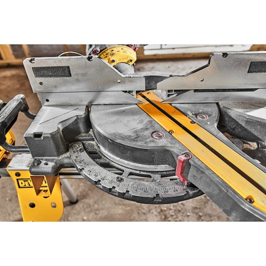 Close-up of a DEWALT miter saw with angular guide and measuring scale for precise woodworking cuts.