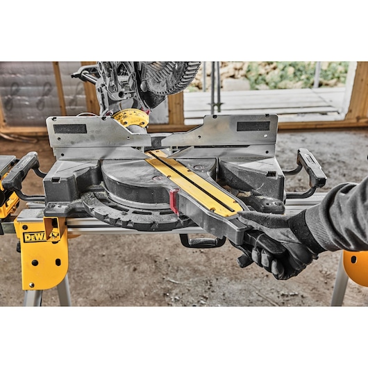 DEWALT miter saw with gloved hand adjusting the saw. Tool is set up indoors for woodworking.