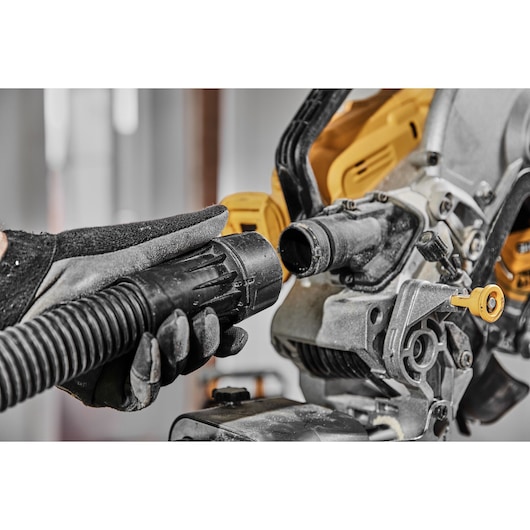 Gloved hand connecting a hose to a DEWALT miter saw dust extraction port.