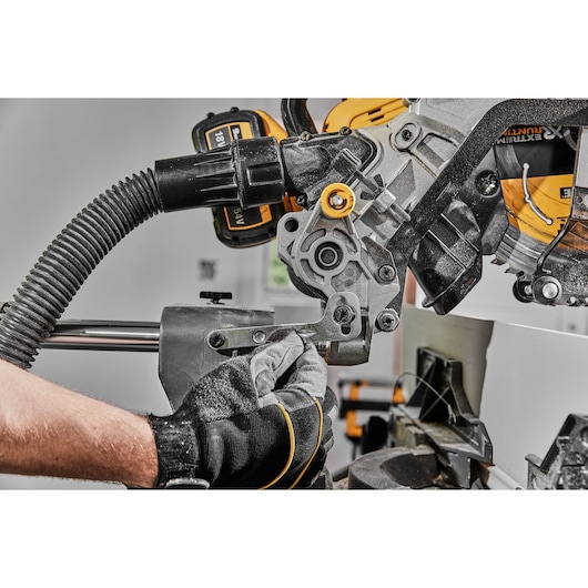 Close-up of a gloved hand adjusting a DEWALT miter saw with dust extraction hose attached.