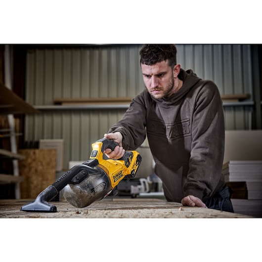 Person using a DEWALT DCV501LN cordless vacuum to clean a wooden workbench in a workshop.