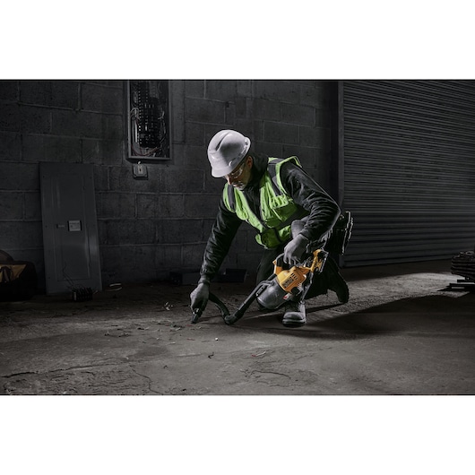 Worker using a DEWALT DCV501LN vacuum to clean debris on a concrete floor in an industrial setting.