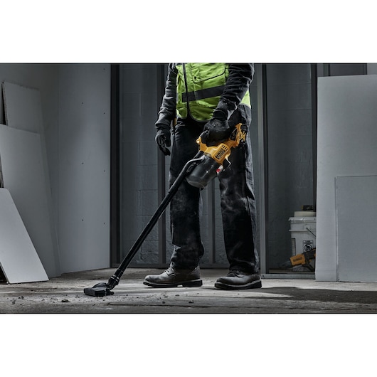 Person using a DEWALT handheld vacuum cleaner on a construction site floor with dust and debris.
