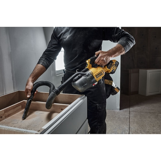 Person uses a DEWALT cordless handheld vacuum to clean dust from a wooden cabinet during construction.