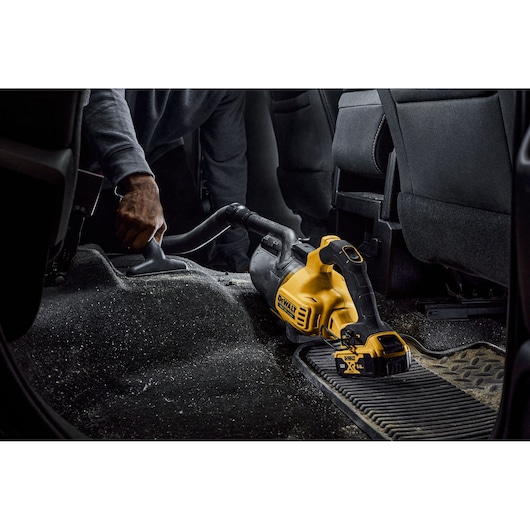 DEWALT cordless vacuum cleaning car interior floor with a person using the nozzle attachment.